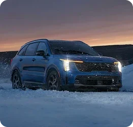 Blue Kia Sorento driving through snow at dusk